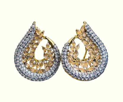 A pair of teardrop-shaped gold earrings paved with clear stones and featuring a central gold leaf pattern, displayed against a solid black background.