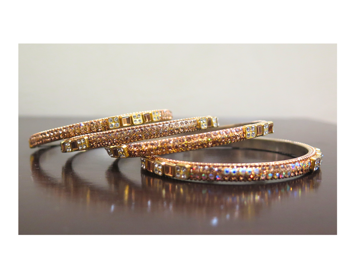 Two rose gold bangles with gemstones on a reflective surface
